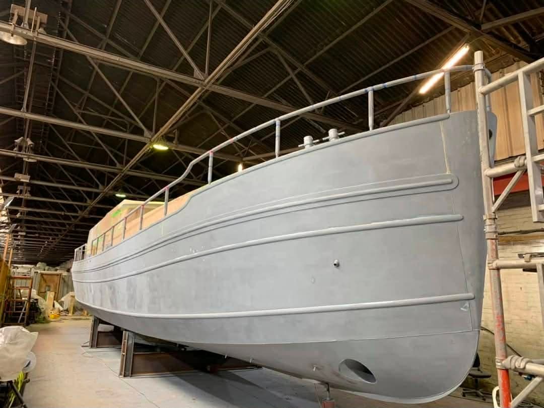 Bare steel hull of a 20 metre river cruiser in a boat shed before coating