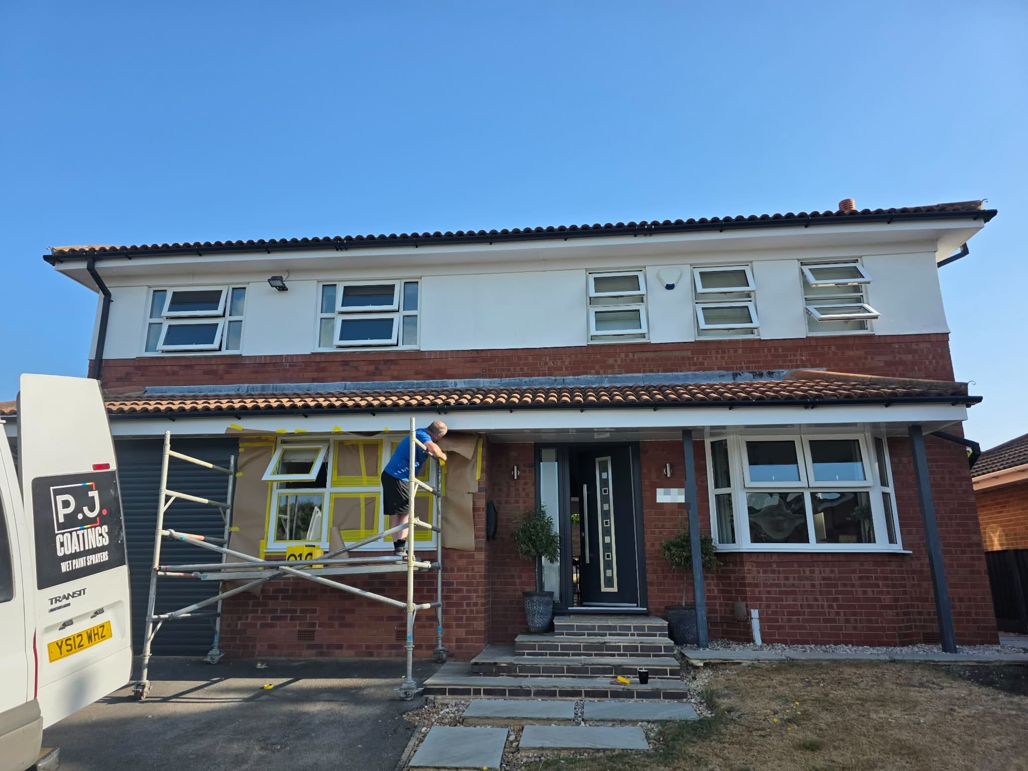 Detached house with white uPVC windows being masked for spraying, with a scaffold tower and the P.J. Coatings van