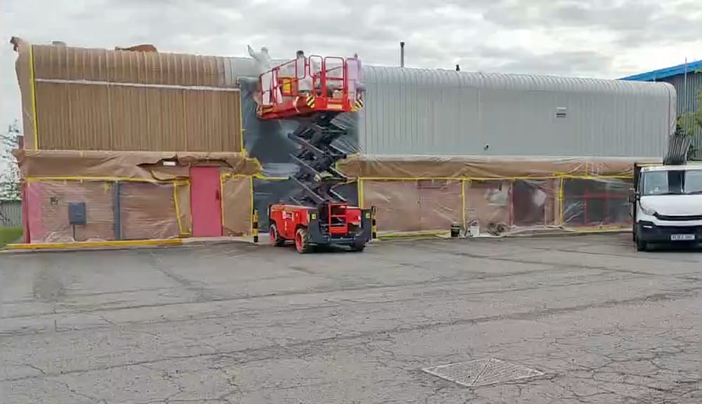 Industrial unit masked and sheeted ready for cladding respraying, with a scissor lift on site